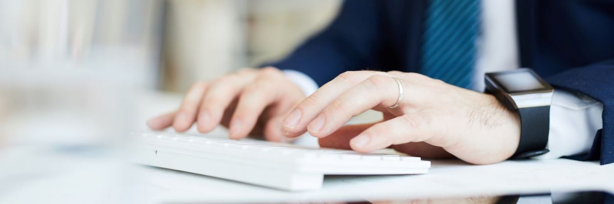 Close-up of unrecognizable businessman in suit sitting at desk and typing on keyboard while preparing business plan on computer