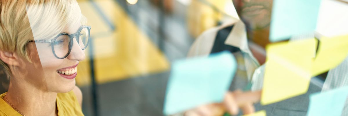 Team of young casual business people collaborating on an creative planning project using a blue and yellow sticky notes in a bright modern office space. Serie with light flares and glass reflections