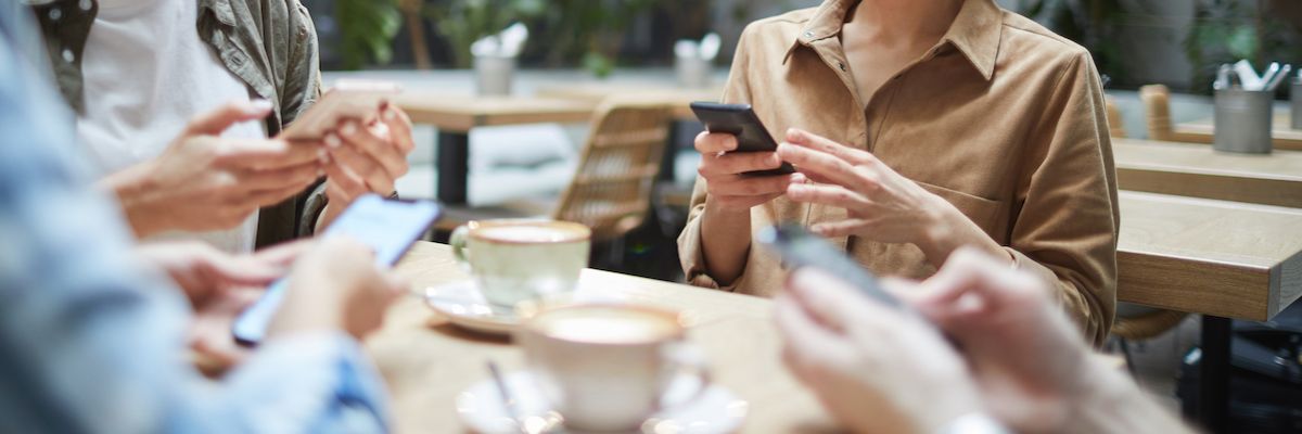 Group of young people sitting at table in cafe and using smartphones in silence